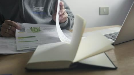 closeup shot, female elder hands go through paper payment bills, desktop office with laptop