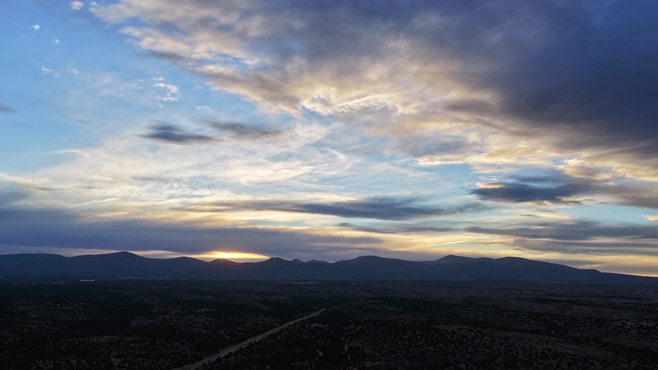Timelapse con drone 4K UHD: un vasto paesaggio arido fa da sfondo a formazioni nuvolose in movimento. La dinamica transizione atmosferica cattura i colori sfumati del crepuscolo e il terreno montuoso scuro con la strada.