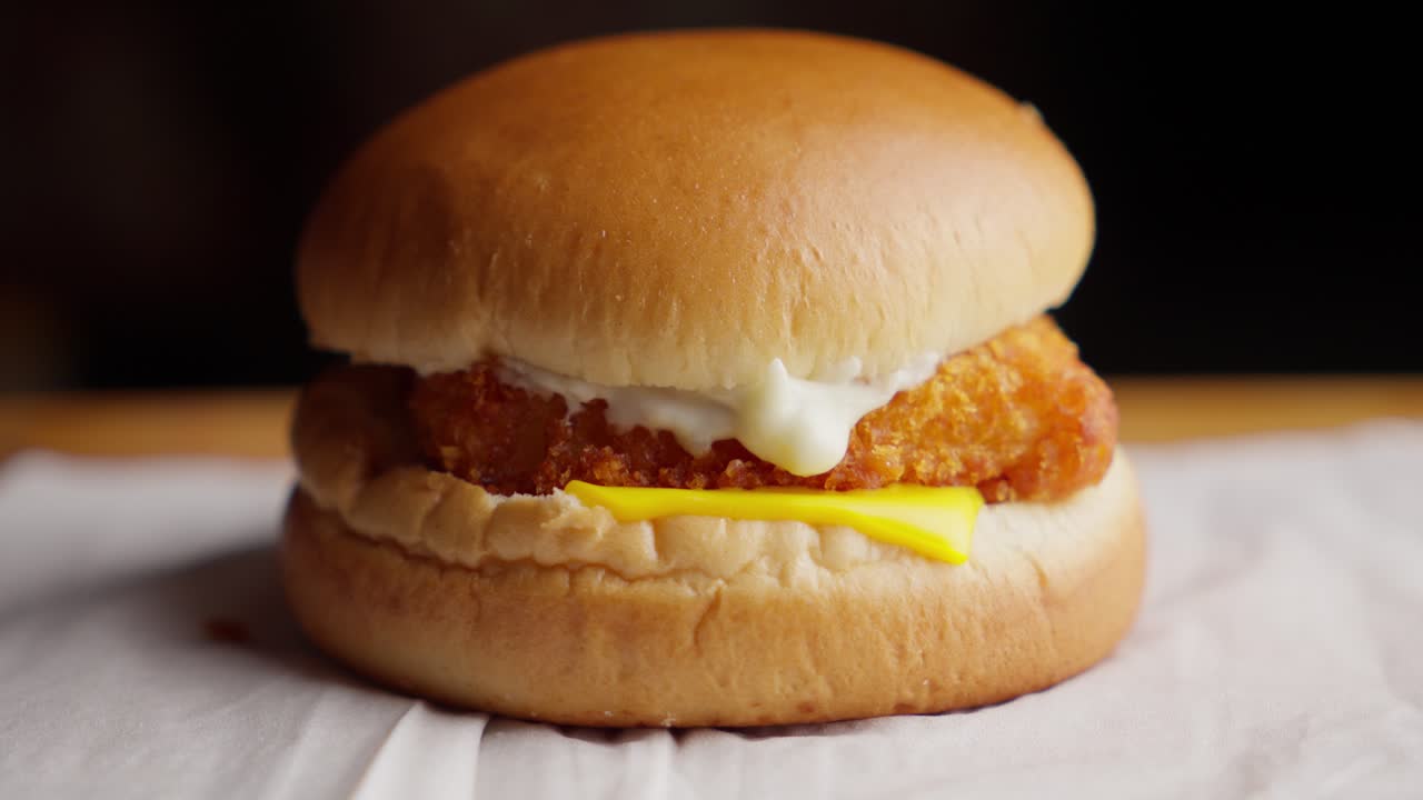 Close-up of hand placing bun on fried fish burger with cheese and mayonnaise