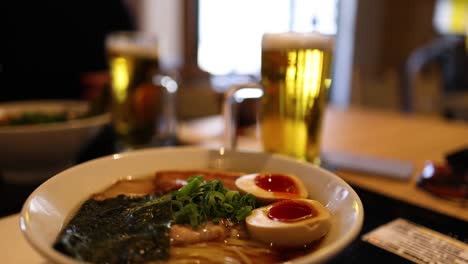 primer plano de un tazón de ramen con bebidas en el fondo