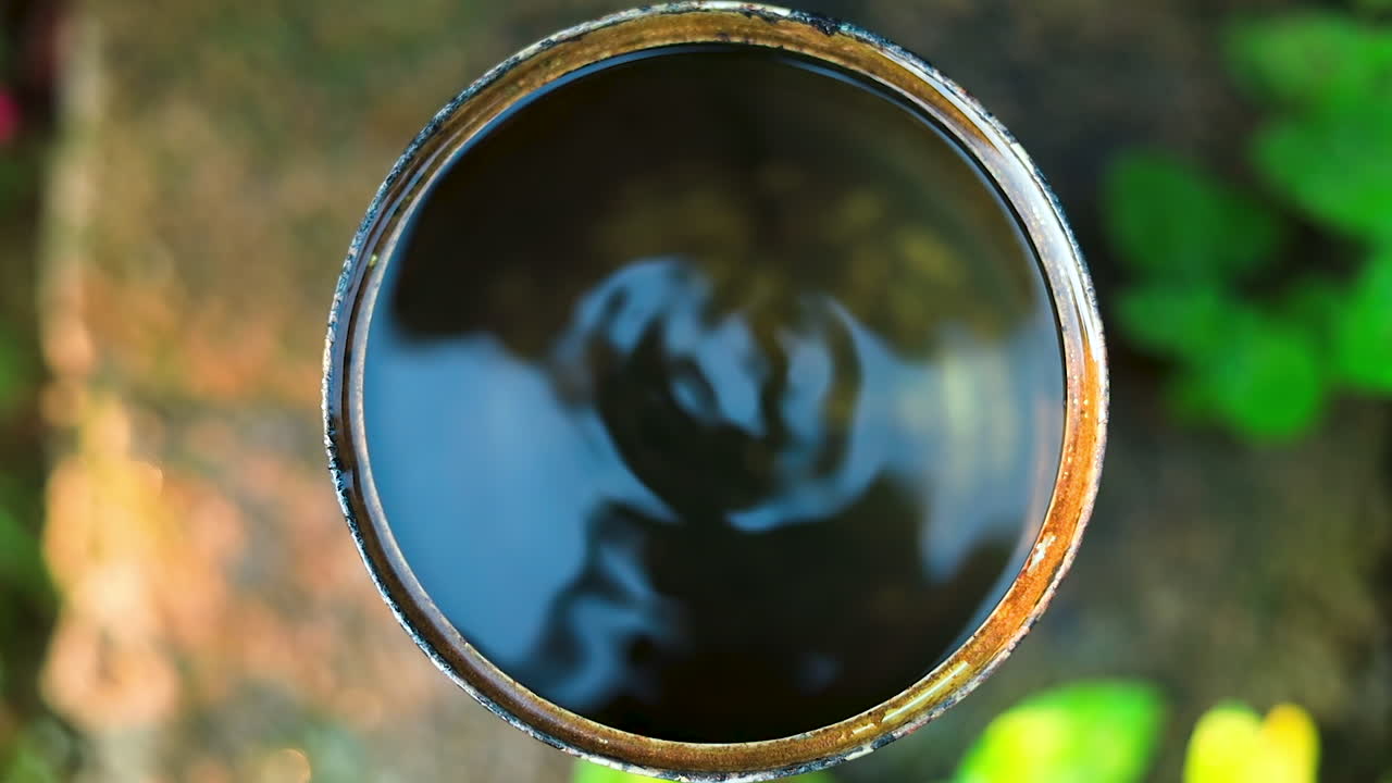 Top view of water leaking from a tap into round container outdoors garden in slow motion.