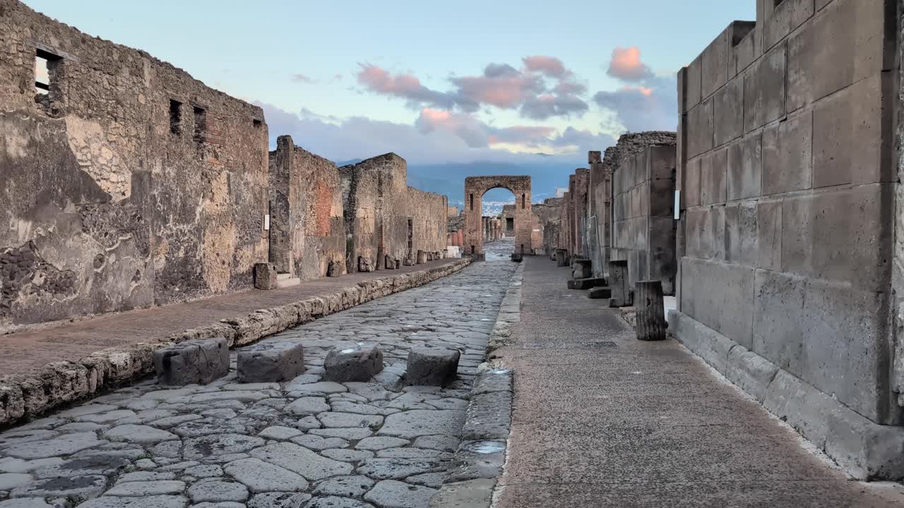 Slow pan left across Pompeii’s ancient stone street at golden hour, showing stepping stones once used to cross flooded roads in the historic Roman city