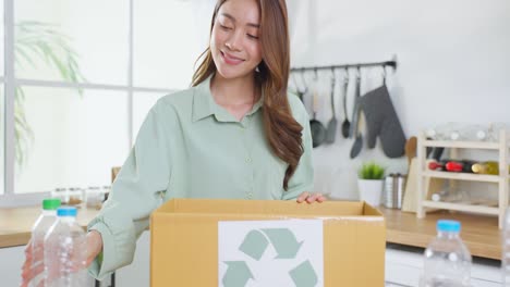 retrato de una mujer asiática que sostiene un contenedor de basura para su reciclaje en casa. una mujer atractiva pone botellas de plástico en una caja de reciclaje para ser ecológica y salvar el medio ambiente.