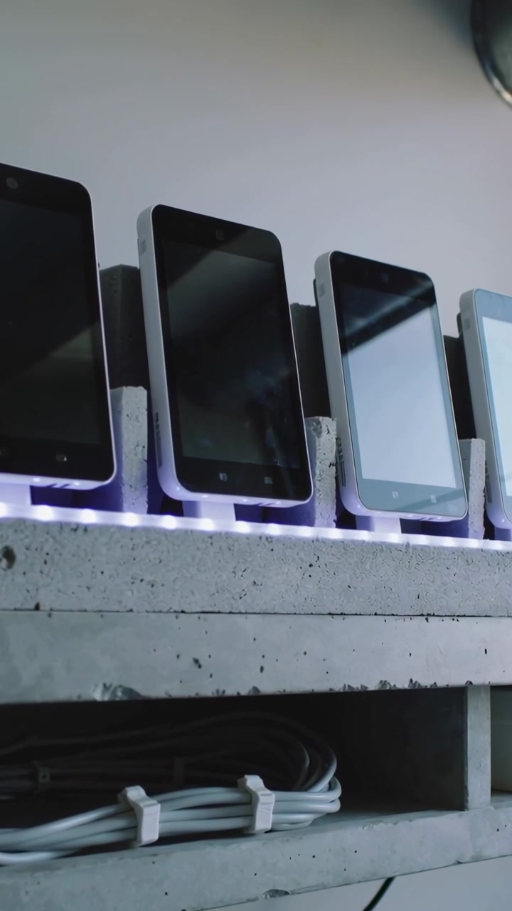 Video verticale: La telecamera si inclina, riprendendo cinque telefoni su uno scaffale con luce LED, rivelando i riflessi.