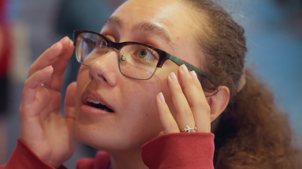 Studentessa latina che si aggiusta gli occhiali, con uno sguardo curioso e un'espressione pensierosa. Ritratti ravvicinati mostrano il profilo e sguardi verso l'alto, con le mani che toccano la montatura durante una prova in boutique, sotto una calda luce interna.