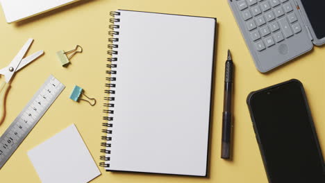 vista aérea de cuadernos, teléfonos inteligentes y papelería escolar sobre un fondo amarillo, en cámara lenta