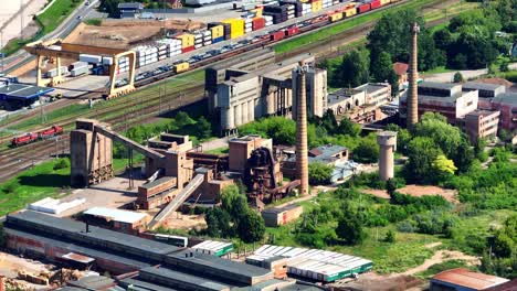 Aerial-view-abandoned-factory,-production-buildings-and-warehouses,-and-tall-chimneys-stand-by-the-railway-tracks