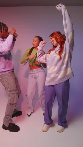 vertical video studio shot of vertical video of group of gen z friends dancing and having fun against pink background