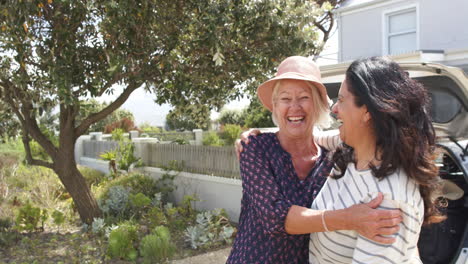 Two-happy-diverse-senior-women-standing-by-car,-laughing-and-embracing-on-sunny-day,-slow-motion