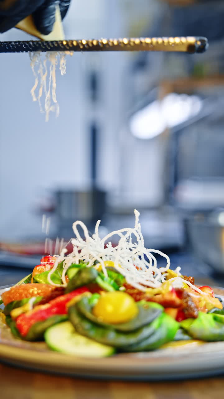 A plate with a tasty dish with lots of greenery. Unrecognized cook grates cheese on top of the food. Close up. Vertical video.