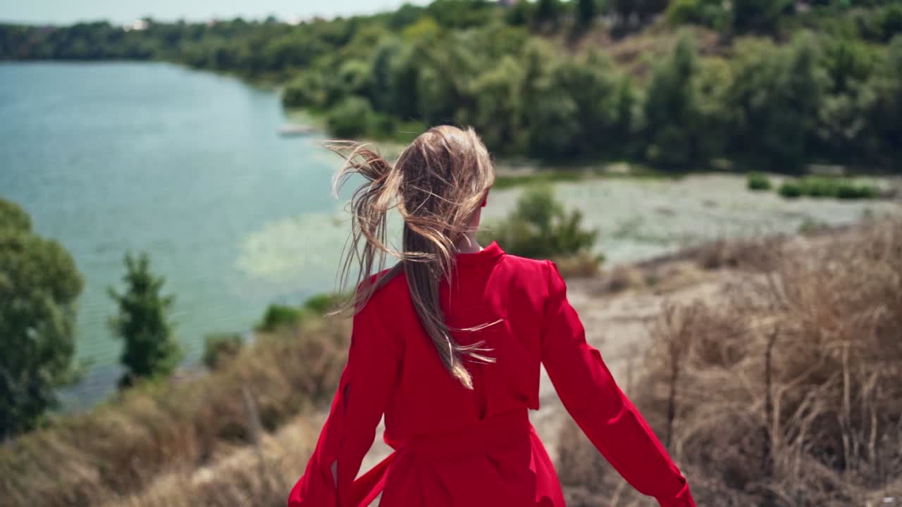Long haired woman on the natural summer background. Beautiful young lady walking down the hill to the river in a sunny day. Slow motion.