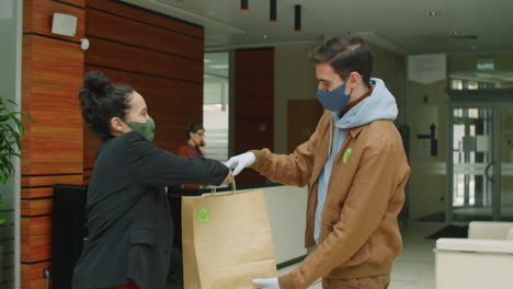 deliveryman in mask and gloves giving paper bag to businesswoman