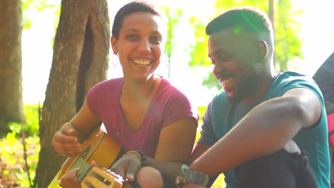 two happy african american people in love spending time outdoors in camp playing guitar and singing