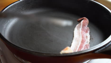 man chef cooking for breakfast slices of bacon, rich in fat and colour, sizzling and smoking in a hot pan