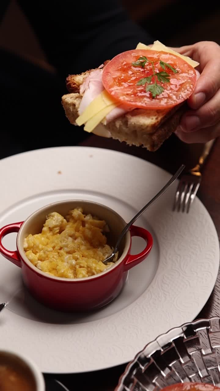 Mano che tiene un panino aperto con uova strapazzate per colazione