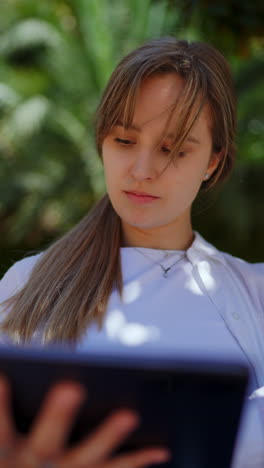 young woman reading on tablet in park