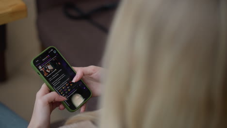 Close-up rear view of young lady seated in modern mall with phone in her hand, scrolling through it, soft focus on screen displaying content, subtle background of urban setting through glass
