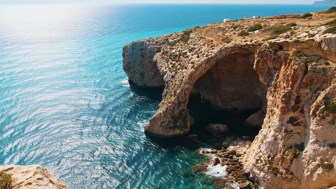 Video verticale: Drone in panoramica che rivela un arco di roccia calcarea e una scogliera sulla costa, con il sole che scintilla sulle increspature.