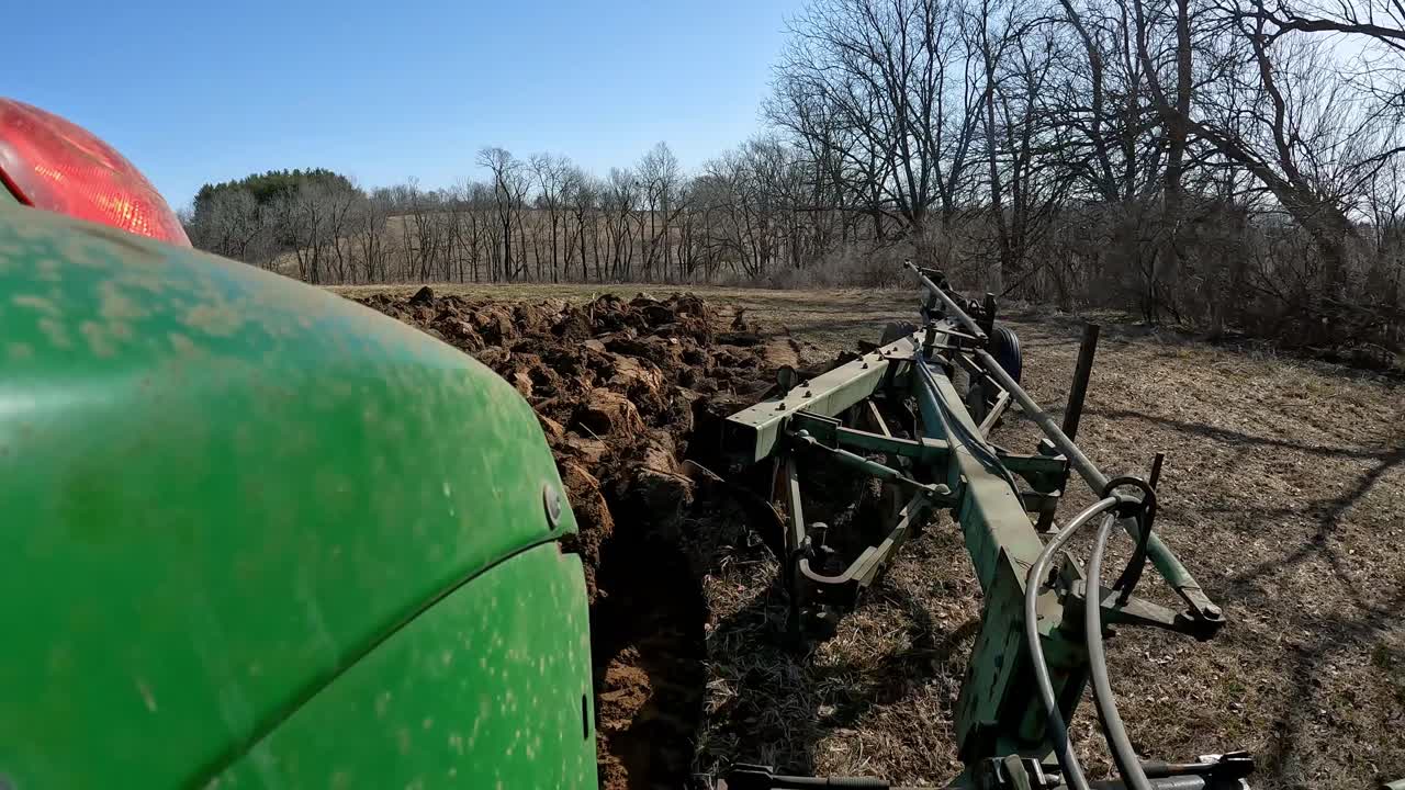 POV - Farmer on green agricultural tractor prepares field for planting and lowers plows at beginning of row