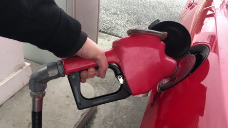 holding a red gas pump as it pumps gasoline fossil fuels into a car