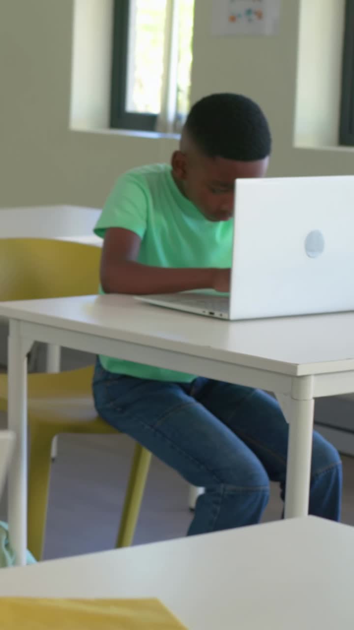 Video verticale: studente in maglietta verde che si china, digita su un laptop alla scrivania di scuola, studiando