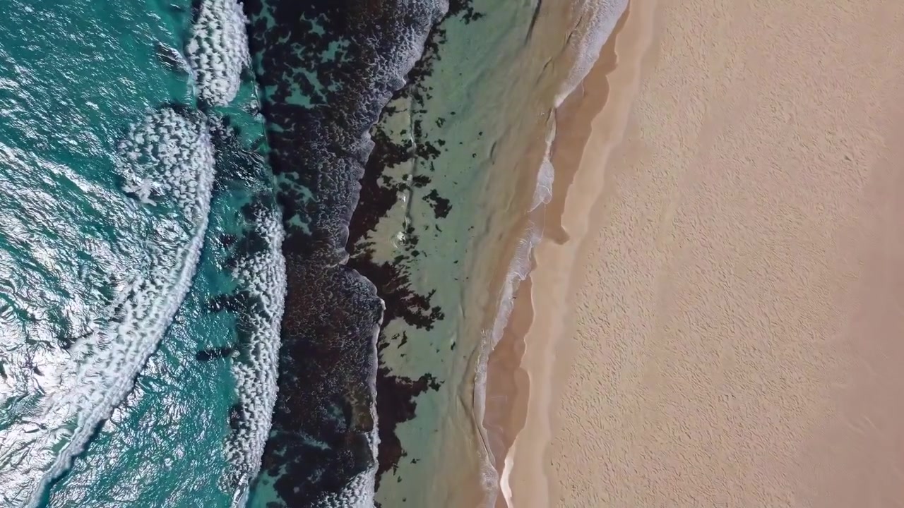 Vista aerea delle onde turchesi dell'oceano che si schiantano sulla spiaggia di Sandy