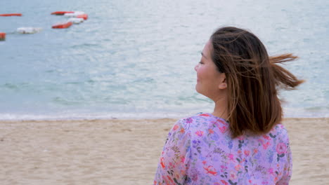 woman on a beach in purple dress waving over someone and looking back