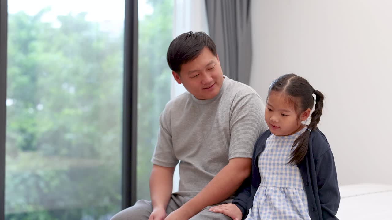 Asian father comforts young daughter in sunlit modern home, expressing support and emotional connection