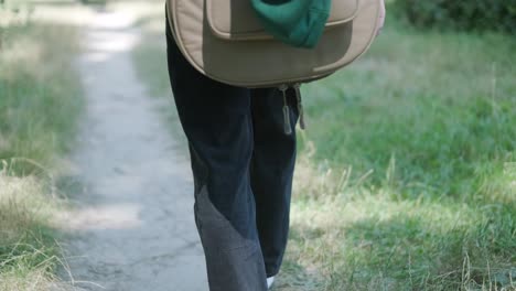 joven caminando con la guitarra en la calle cerca del bosque