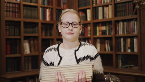 portrait of a 11-year-old girl with a textbook, stands against the background of bookshelves in the library