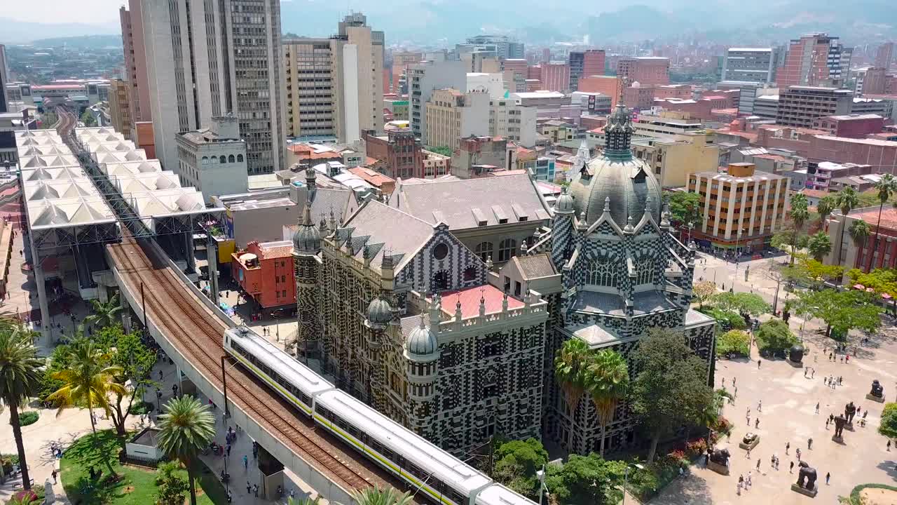 Bela vista aérea de trem do metrô passando pela Praça Botero ao entrar na estação em dia ensolarado.