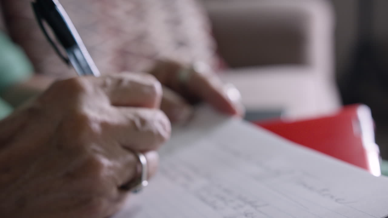 Elderly woman carefully writes in notebook with pen (closeup on hand)