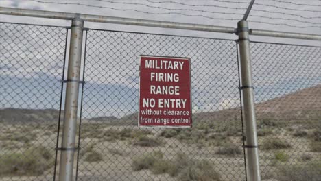 high quality 3d cgi render with a smooth dollying-out shot of a chainlink fence at a high security installation in a desert scene, with a military firing range no entry sign