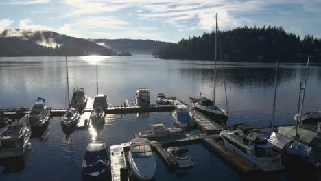 Multiple-sailing-yachts-moored-at-a-wooden-scaffolding-in-a-marina-with-islands-in-the-Indian-Arm-bay-at-background-on-a-sunny-day