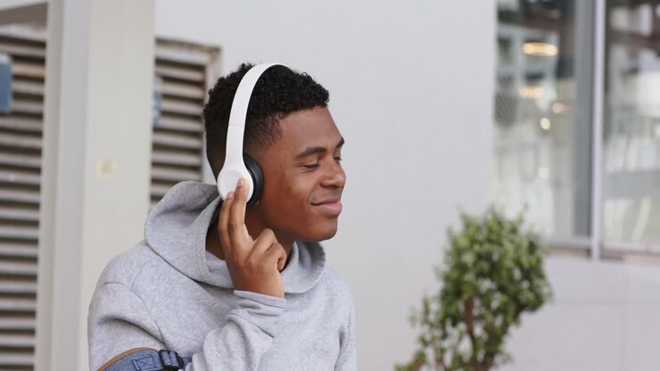 Uomo con zaino che preme il padiglione della cuffia, avviando la musica e annuendo fuori dall'ingresso, con spazio per il testo.