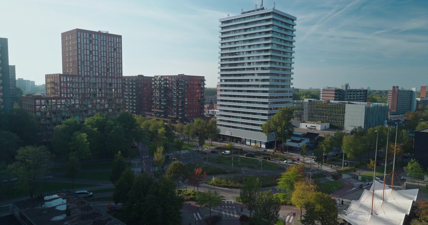 Bairro urbano com um edifício alto e prédios residenciais de tijolos com varandas de vidro, árvores, rotatória, cruzamento e tráfego, Países Baixos, Holanda