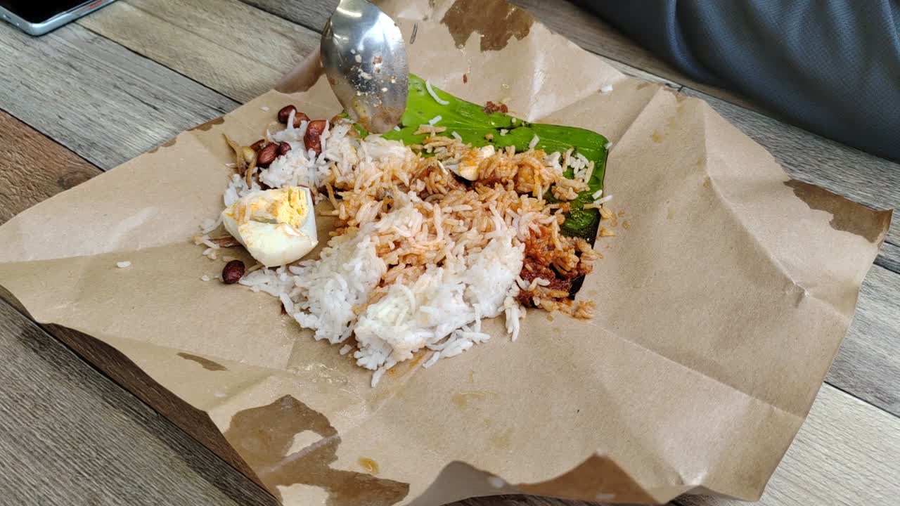 A woman enjoys nasi lemak bungkus, Malaysia's popular, quick breakfast. This simple meal, with egg and sambal, comes conveniently wrapped in paper for easy portability