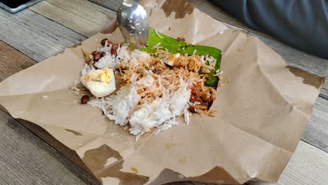 a woman enjoys nasi lemak bungkus, malaysia's popular, quick breakfast. this simple meal, with egg and sambal, comes conveniently wrapped in paper for easy portability