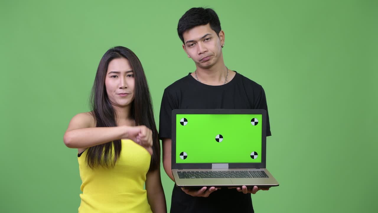 Young Asian couple showing laptop and giving thumbs down