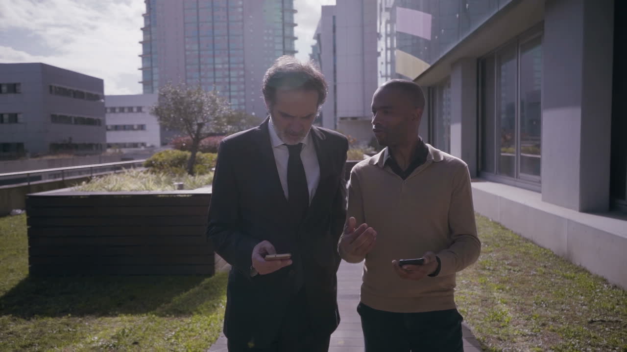 Smiling businessmen using smartphones and walking in slow motion