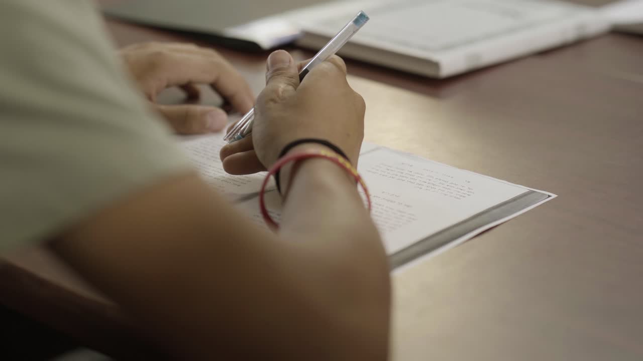 A student tries to answer a test, Close-Up on the hand,
The student plays with the pen,
Hebrew language test