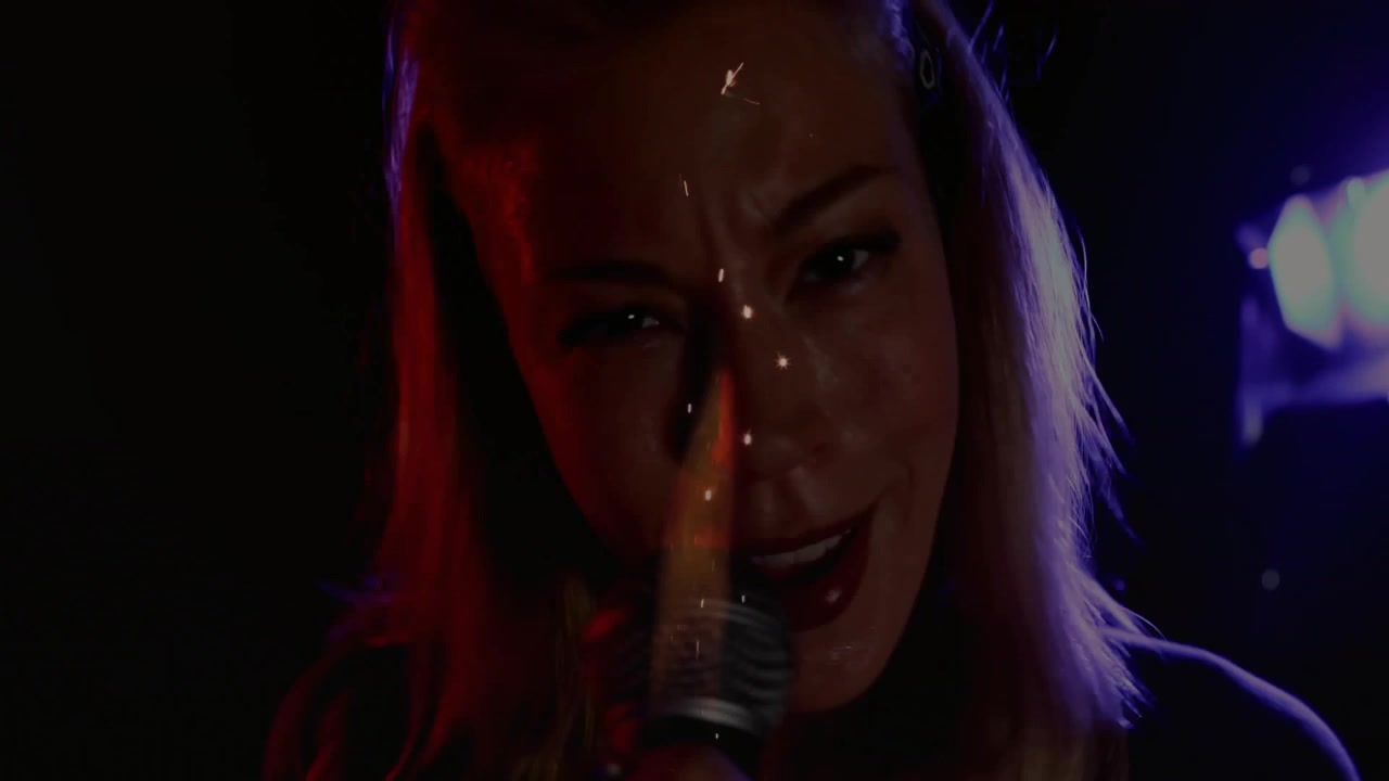 Scintilla musicale che si eleva sotto una luce rosso porpora e telecamera dinamica che zooma sul cantante che tiene il microfono e canta