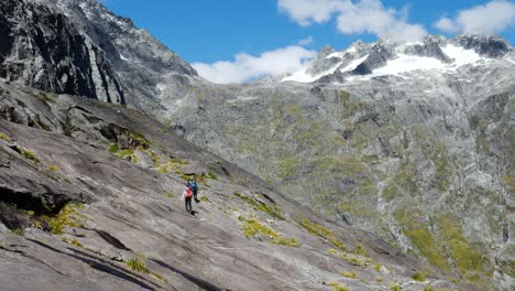 grupo de excursionistas caminando en la montaña rocosa en el camino de la silla de montar de gertrude en el parque nacional de fiordland durante el verano - picos nevados de la montaña en el fondo
