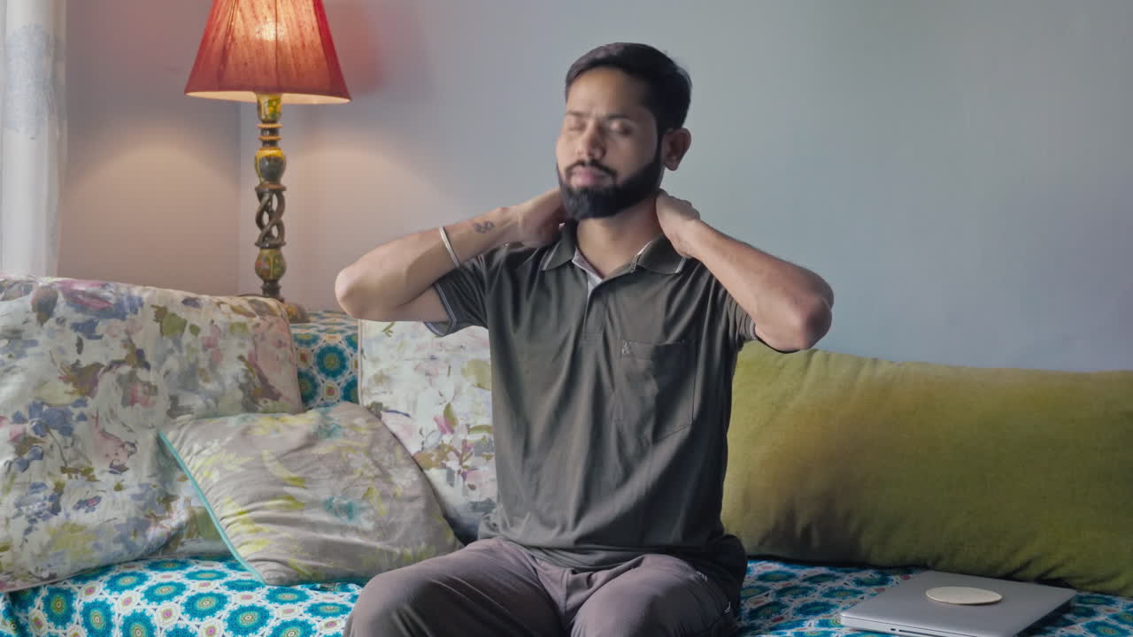 A man sitting on a sofa feeling severe neck pain.