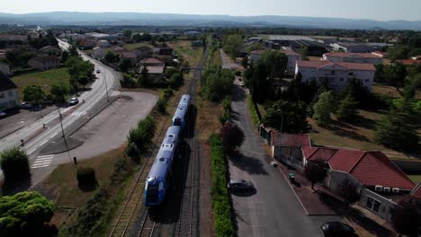 Drohnenaufnahme-Eines-Regionalzuges,-Der-Den-Bahnhof-In-Der-Französischen-Landschaft-Verlässt,-Département-Loire,-Region-Auvergne-Rhône-Alpes,-Frankreich