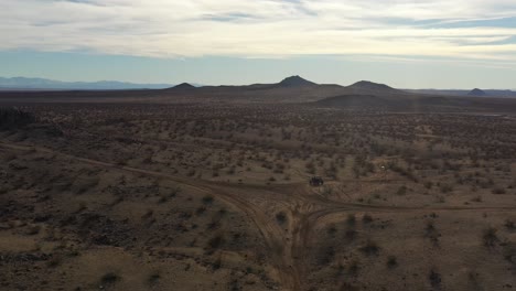 Conducir-Un-Vehículo-Fuera-De-La-Carretera-Por-Una-Pendiente-Empinada-Para-Revelar-El-Terreno-Accidentado-Del-Desierto-De-Mojave---Vista-Aérea