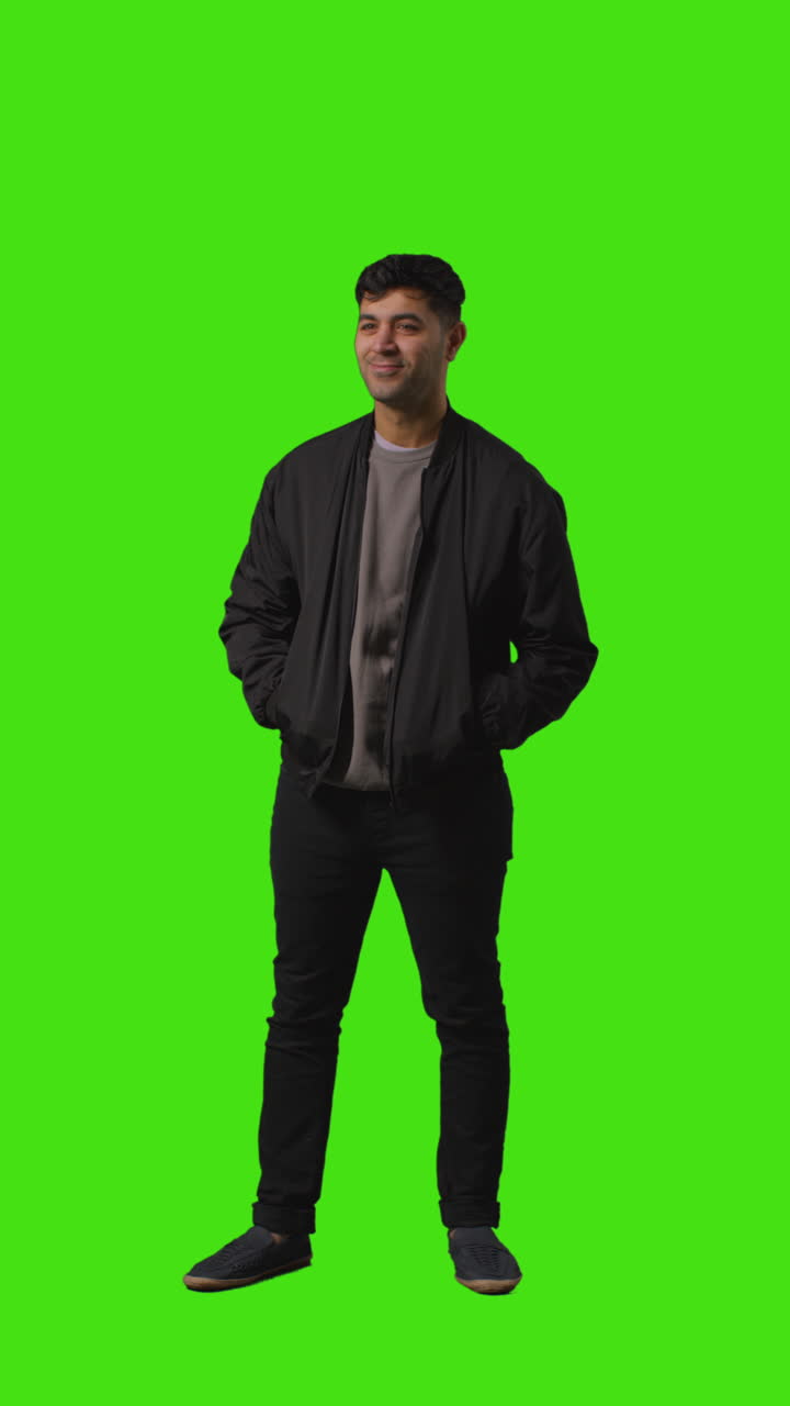 손을 주머니에 넣고 녹색 화면 앞에 서 있는 캐주얼하게 옷을 입은 젊은 남자의 수직 비디오 전체 길이
