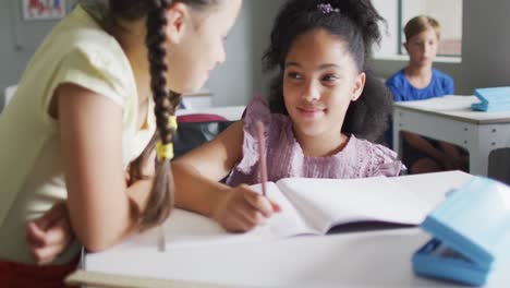 Video-of-happy-diverse-girls-at-desk-doing-lessons-together-in-classroom