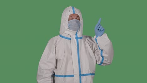 portrait of a man in a protective suit and medical mask looks at the camera and points his fingers to the side, up and down. green screen, chroma key. slow motion. close up