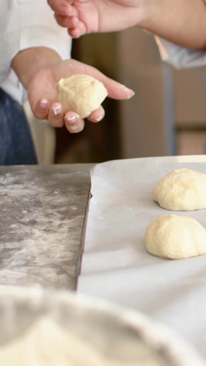 Vertical video: Shaping hands in dark apron pressing dough on floured counter to tray for baking